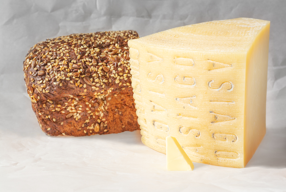 O bucată mare de brânză asiago pe un tocător de lemn
