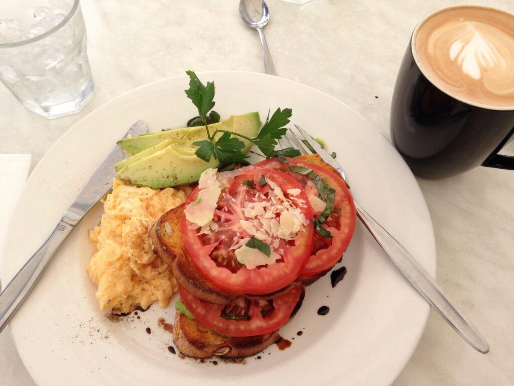 O farfurie cu micul dejun australian care include avocado, ouă și roșii alături de o cană de cafea