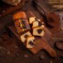 Un chec de post dens și aromat, feliat și așezat pe un tocător, alături de linguri din lemn cu pudră de cacao
