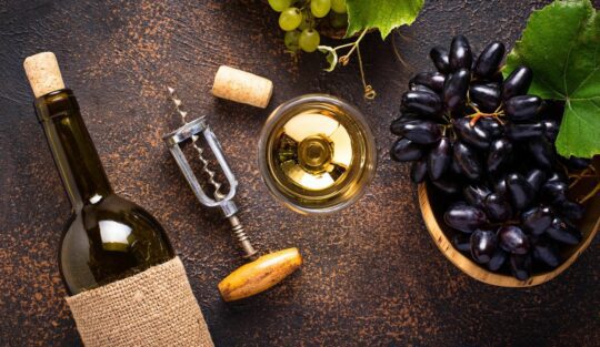 O masă cu o sticlă de vin alături de un tirbușon pentru a ilustra cum să desfaci o sticlă de vin