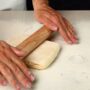 O femeie care întinde pe blatul de lucru aluatul franțuzesc pentru croissante cu sucitorul