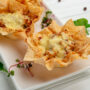 Două coșulețe din foietaj umplute cu carnaciori si brânză puse pe o farfurie albă și ornate cu verdețuri