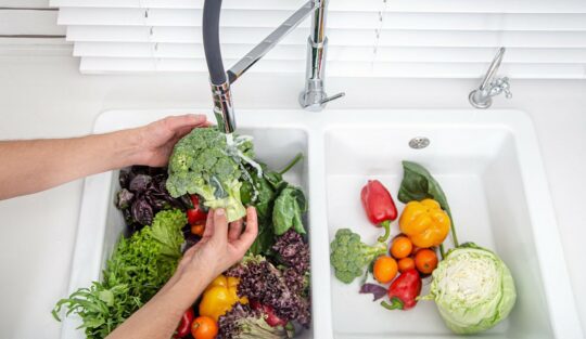 O femeie care curăță salata la chiuvetă pentru a ilustra câteva alimente pe care nu e recomandat să le speli