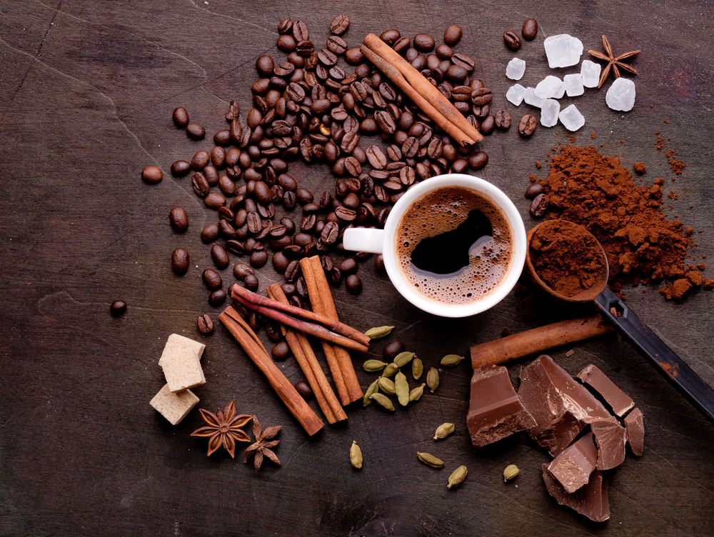 Condimente pentru cafea pe o masă de lemn alături de o ceașcă de cafea