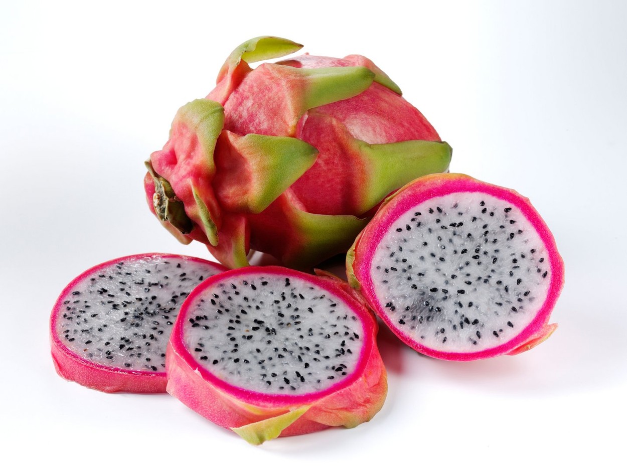 Un fruct al dragonului întreg, alături de felii de pitaya, așezate pe o suprafață de culoare albă
