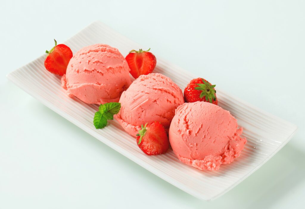 Înghețată de căpșuni cu rubarbă servită pe un platou alb și decorată cu frunzulițe de mentă
