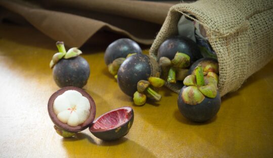 Fructe de mangostan întregi și secționate în jumătate, așezate pe masă.