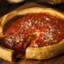 O pizza Chicago așezată pe un tocător, din care a fost tăiată o bucată