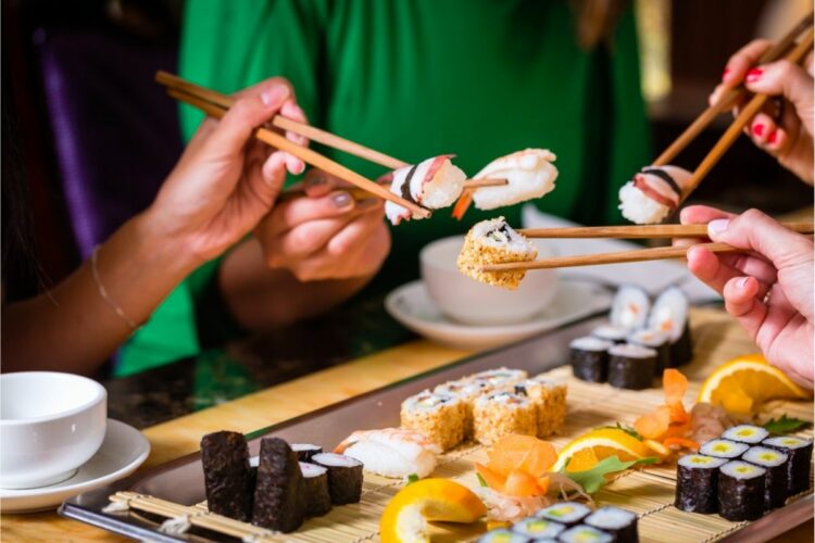 Oameni mâncând sushi în restaurant, la o masă cu mai multe feluri de mâncare