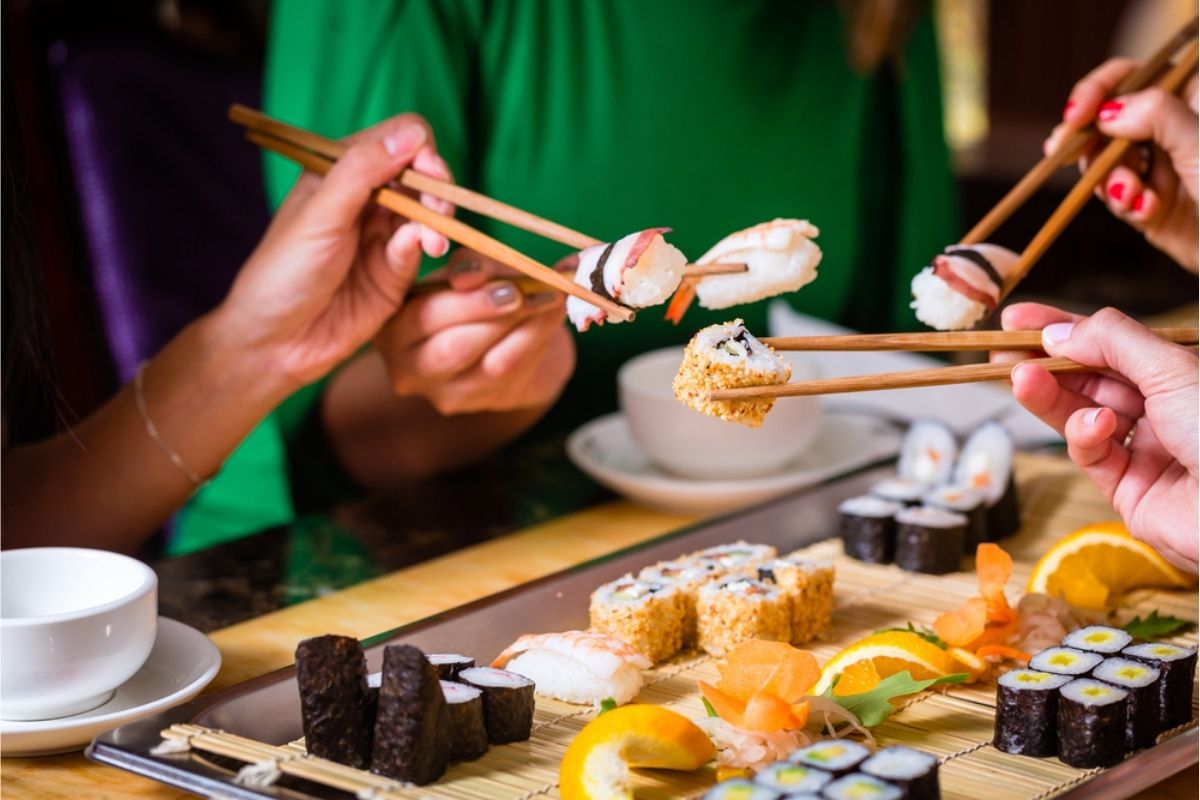 Oameni mâncând sushi în restaurant, la o masă cu mai multe feluri de mâncare