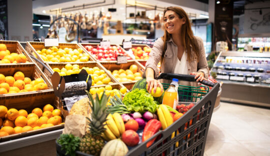 O femeie care are un cărucior de cumpărături plin cu fructe și legume
