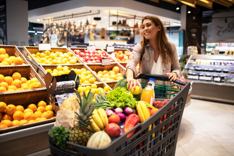 O femeie care are un cărucior de cumpărături plin cu fructe și legume