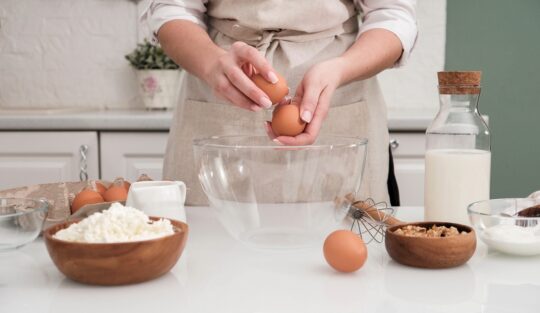 O femeie frumoasă care pregătește prăjituri cu ouă într-un bol