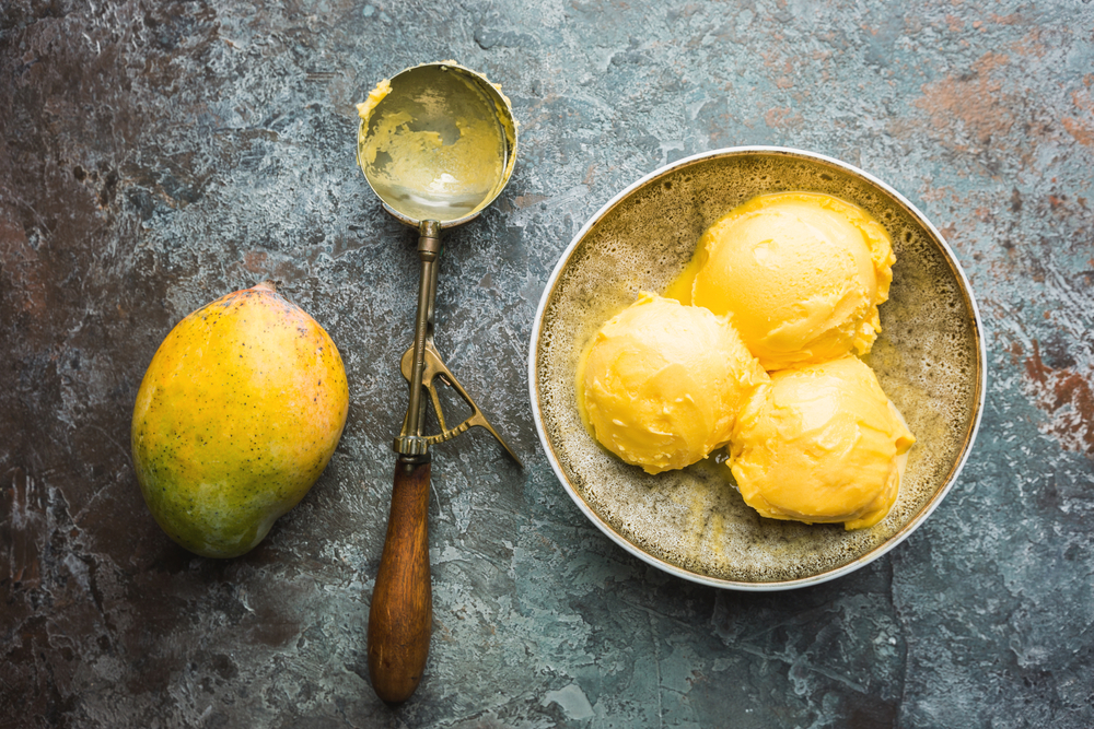 Înghețată de mango fără zahăr servită într-un bol alături de o lingură aurie