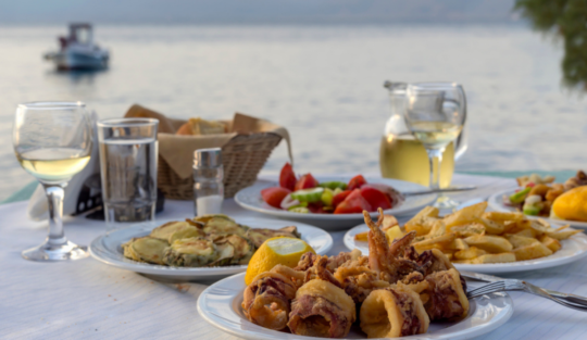 O masă cu preparate tradiționale din Grecia, la un restaurant local, la malul mării