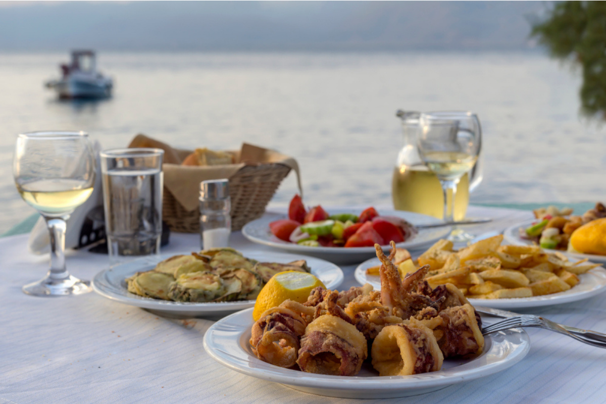 O masă cu preparate tradiționale din Grecia, la un restaurant local, la malul mării