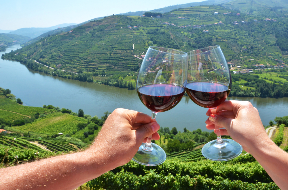 Două persoane care ciocnesc două pahare de vin în fața valei Douro