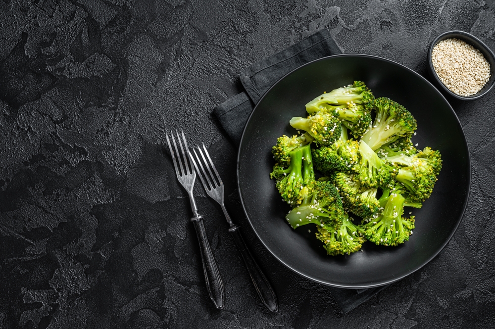 Un blat negru pe care se află o farfurie cu broccoli alături de o furculiță