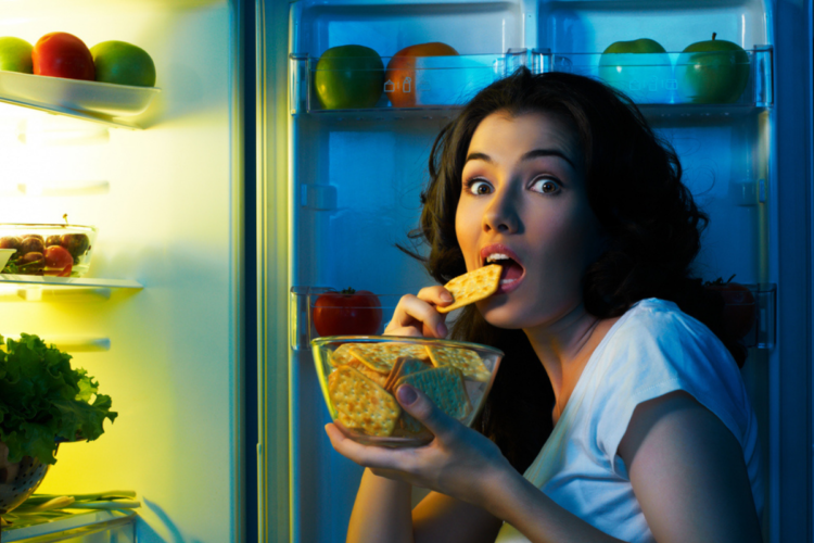 O femeie care mănâncă noaptea o gustare, la lumina frigiderului