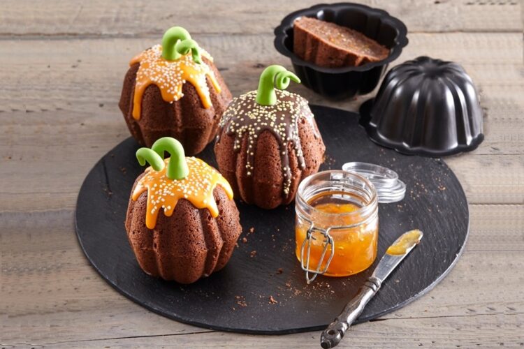 Muffins fantezie sub forme de dovleci pe un platou negru, alături de un borcan cu jeleu și un cuțit