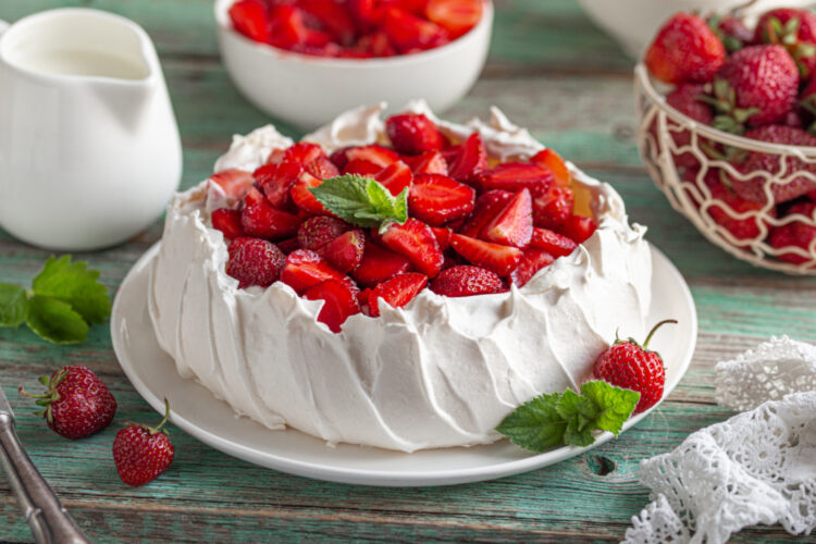 Un tort pavlova cu căpșuni, așezat pe o farfurie albă, întinsă
