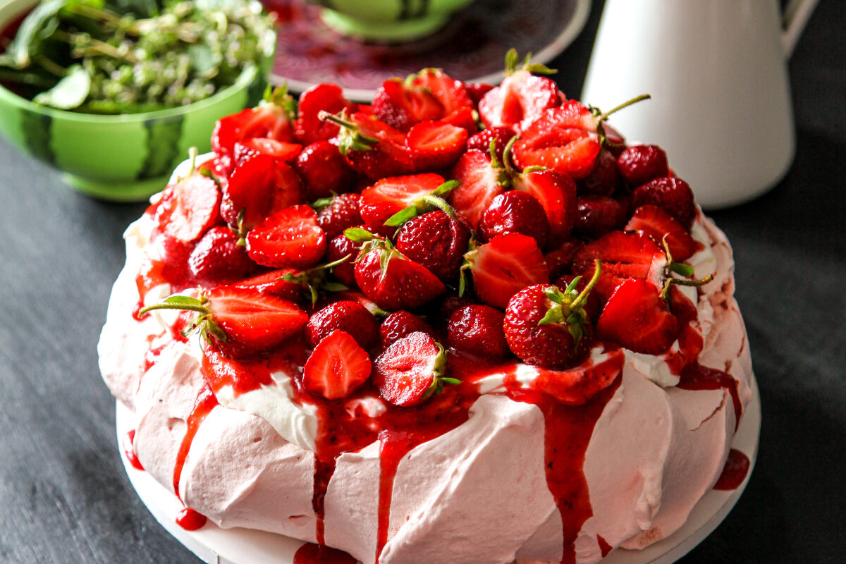 O prăjitură pavlova, decorată cu căpșuni și sos de coacăze roșii