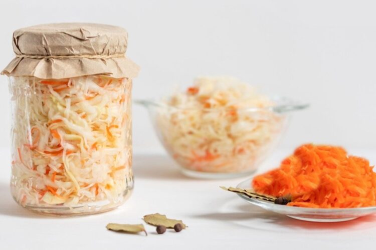 Borcan și bol cu salată de morcovi cu varză, alături de o farfurie cu morcovi răzuiți