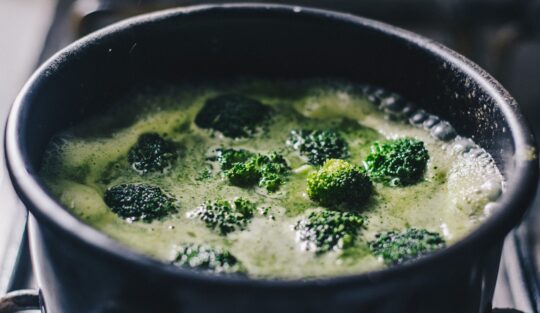 Oală neagră cu bucăți de broccoli în apă pentru fiert