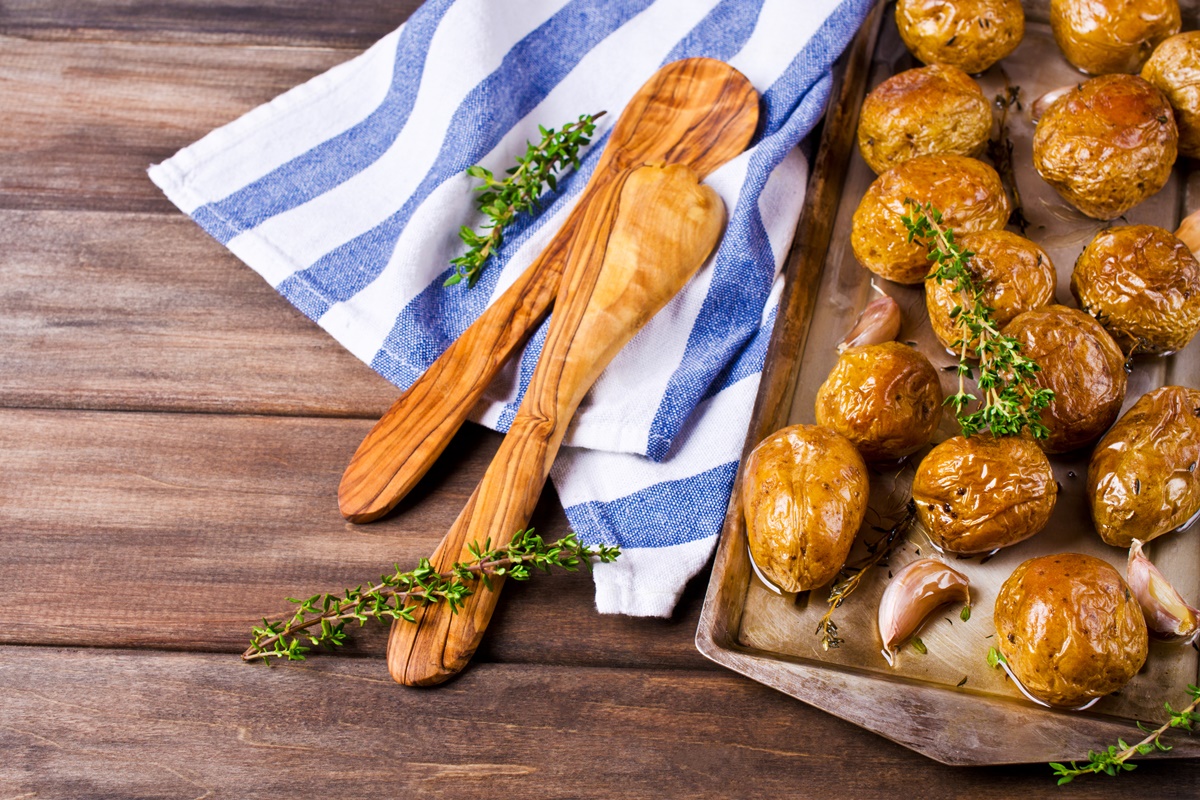 Cartofi întregi la cuptor în tavă cu usturoi și cimbru, alături de două tacâmuri de lemn
