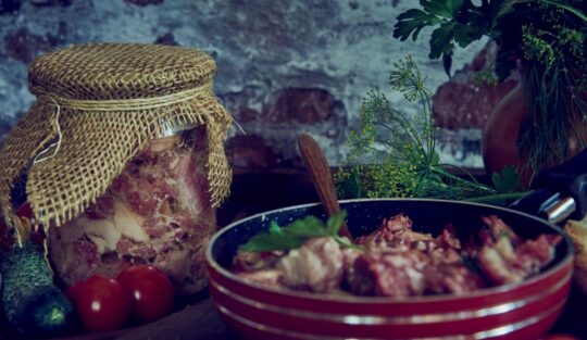 Un bol roșu în care se află carne de vită gătită alături de un borcan plin cu confit