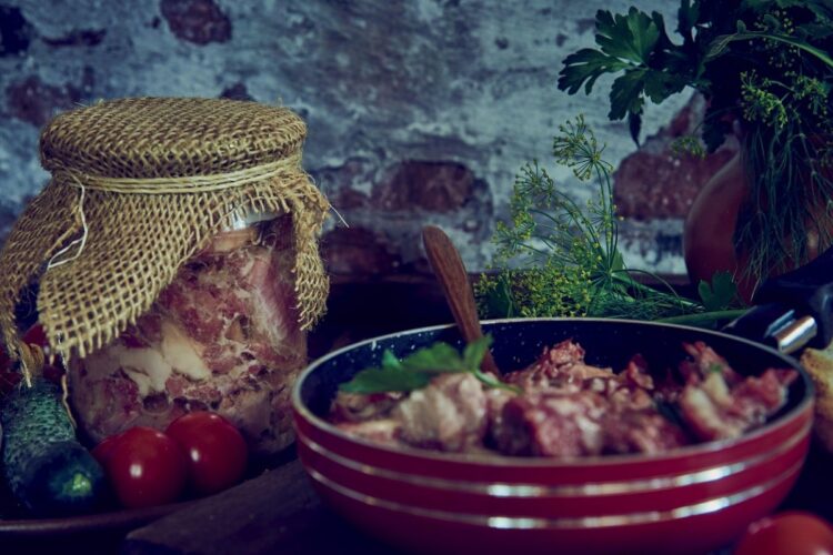 Un bol roșu în care se află carne de vită gătită alături de un borcan plin cu confit