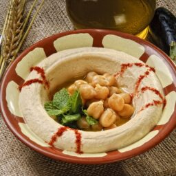 Hummus cu vinete în bol rustic, decorat cu boabe de năut și frunze de pătrunjel verde