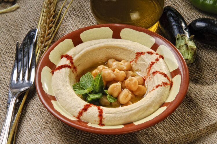 Hummus cu vinete în bol rustic, decorat cu boabe de năut și frunze de pătrunjel verde