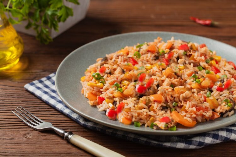 Porție de orez cu sos de roșii și legume într-o farfurie de culoare gri așezată pe un ștergar în carouri albastre