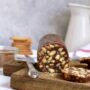 Salam de biscuiți cu nuci porționat pe un tocător de lemn, alături de o carafă albă