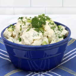 Salată de conopidă cu maioneză și usturoi în bol albastru pe un ștergar albatru cu carouri albe