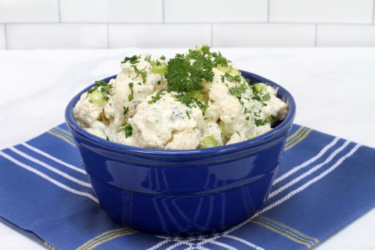 Salată de conopidă cu maioneză și usturoi în bol albastru pe un ștergar albatru cu carouri albe