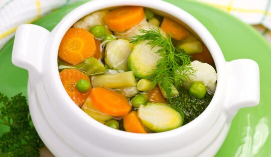 Vas alb cu supă din multe legume printre care morcov și conopidă