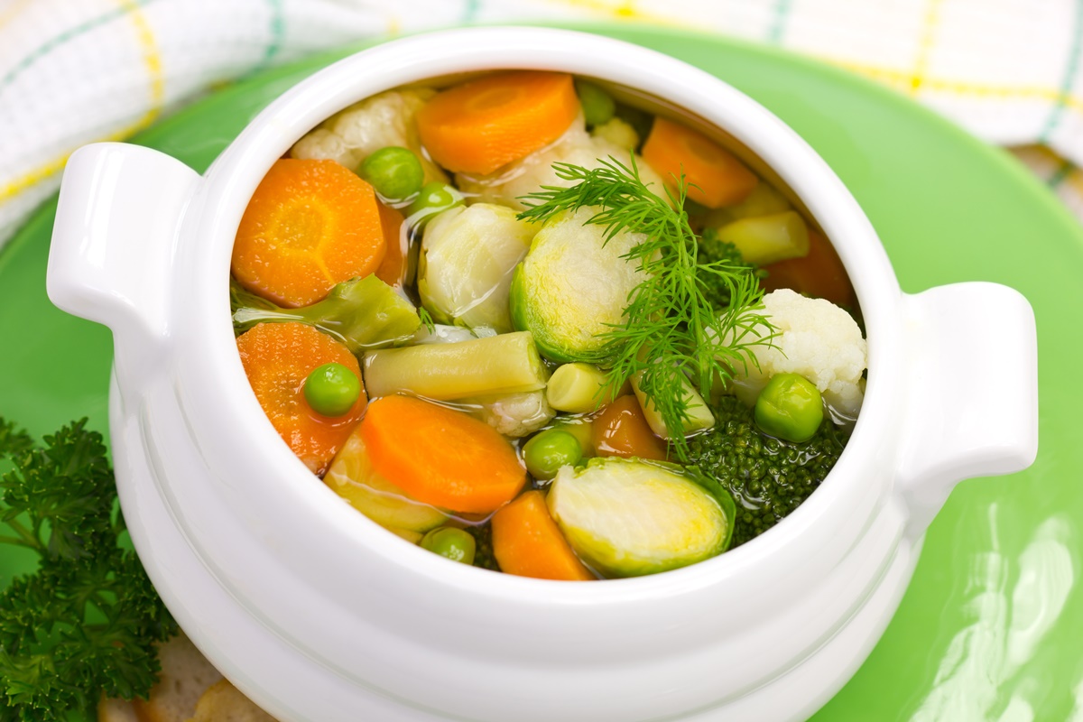 Vas alb cu supă din multe legume printre care morcov și conopidă