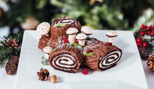 Tort Buturuga de Crăciun sau Bûche de Noël decorat cu fursecuri ciupercuțe și prezentat într-un decor de sărbătoare