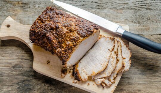 Pastramă de porc preparată la cuptor, porționată pe un tocător de lemn alături de un cuțit