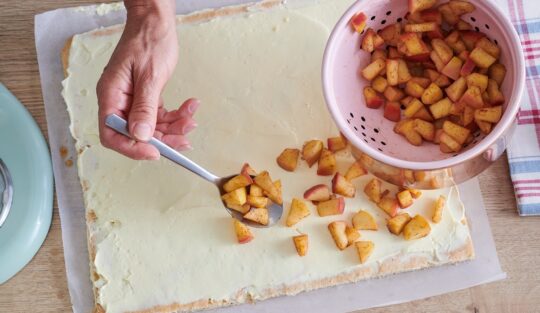 Pasul de adăugare a cuburilor de mere caramelizate peste foaia de ruladă cu cremă de vanilie