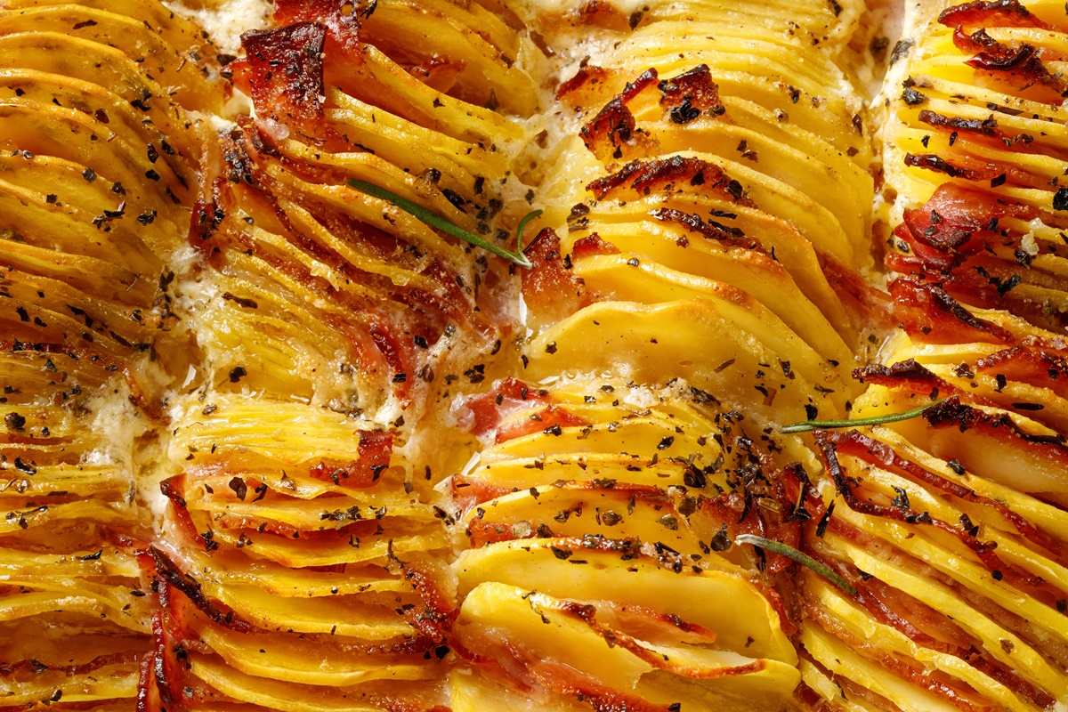 Cartofi feliați subțire și împănați cu felii de șuncă și brânzî, preparați la cuptor
