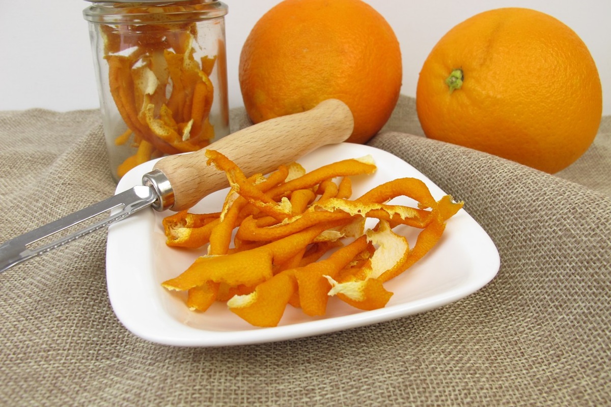 Coji de portocale în borcan și în farfurie, alături de dispozitiv de curățare și două portocale