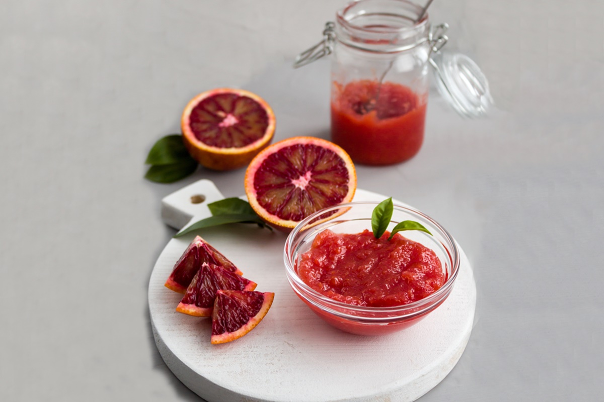 Dulceață de portocale roșii în borcan și în bol, alături de portocale secționate