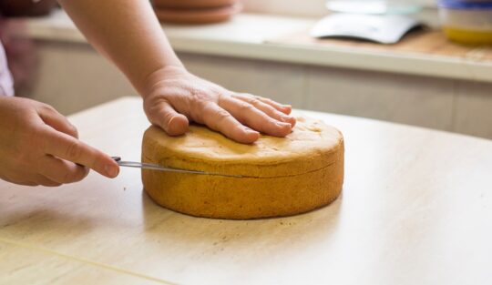 Femeie secționând blatul de tort cu un cuțit
