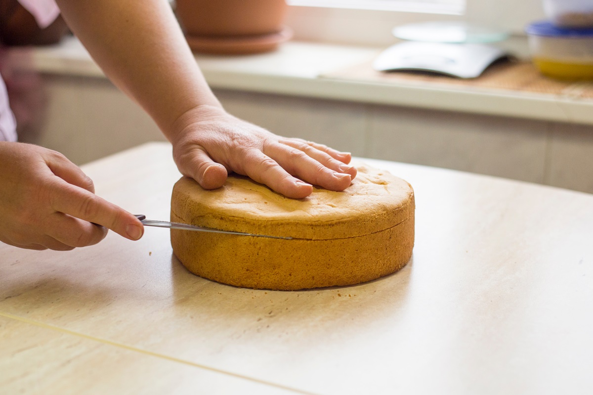 Femeie secționând blatul de tort cu un cuțit