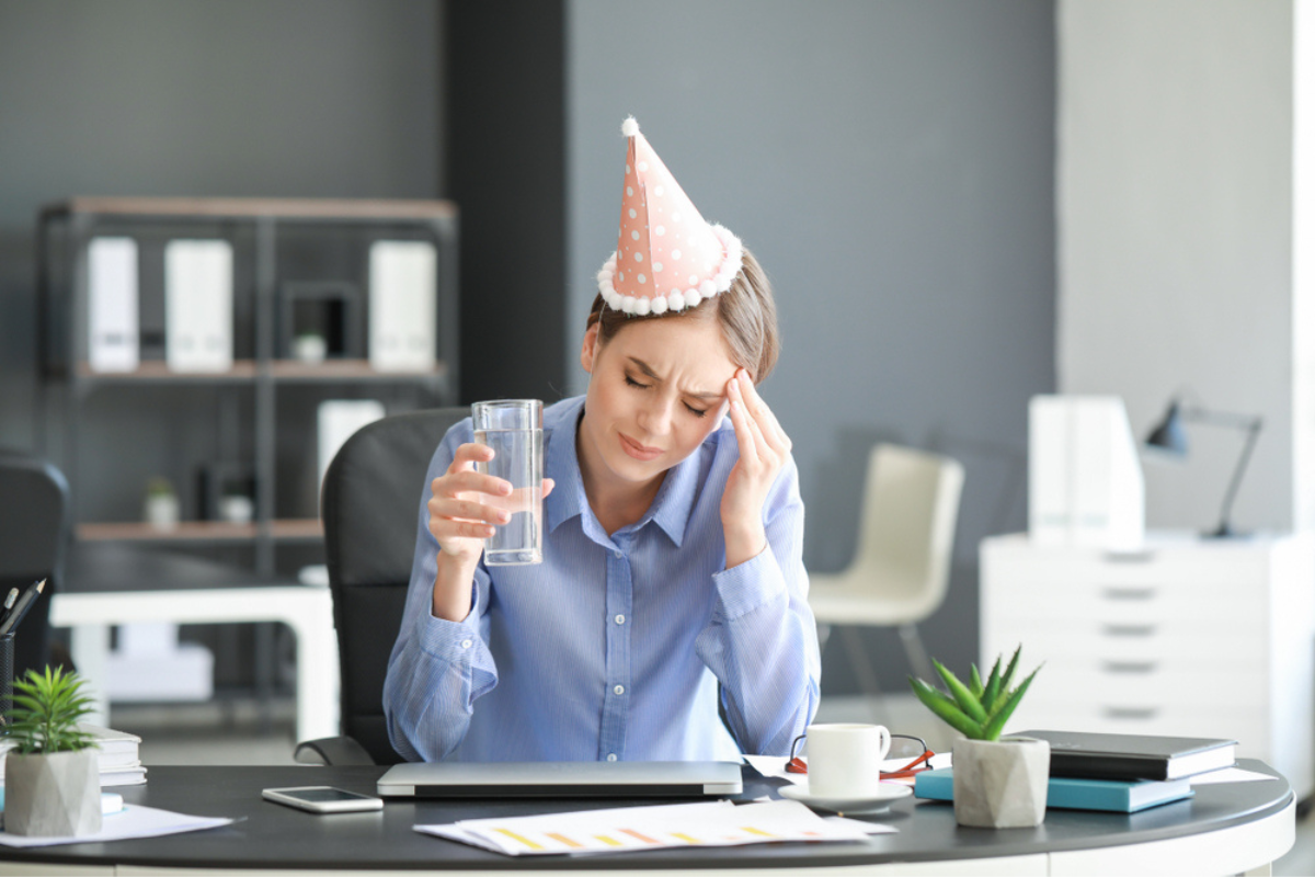 O femeie care stă la masă cu o pălărie de petrecere pe cap și încearcă remedii antimahmureala
