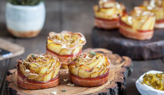 Șase trandafiri crocanți din cartofi cu bacon pe platouri rustice de lemn, alături de un bol cu salată de murături