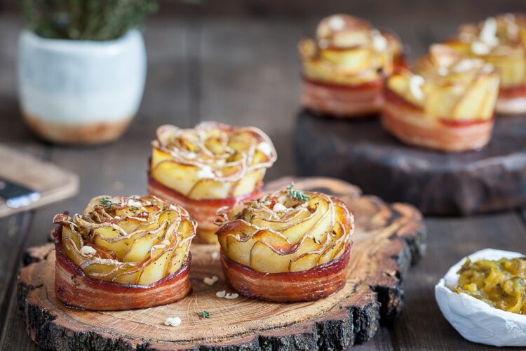 Șase trandafiri crocanți din cartofi cu bacon pe platouri rustice de lemn, alături de un bol cu salată de murături